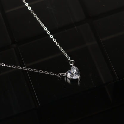 A silver necklace featuring a heart-shaped pendant, displayed on a reflective surface.